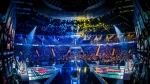 The image captures an electrifying moment at the Intel Extreme Masters (IEM) Katowice, an iconic esports tournament held in a large arena filled to capacity with spectators. The view shows multiple gaming teams competing on stage, surrounded by massive digital displays and vibrant lighting that contribute to a dynamic and immersive viewing experience. The audience, awash in colorful lights, adds to the atmosphere of high-stakes competition, highlighting the event's popularity and significance in the esports world.